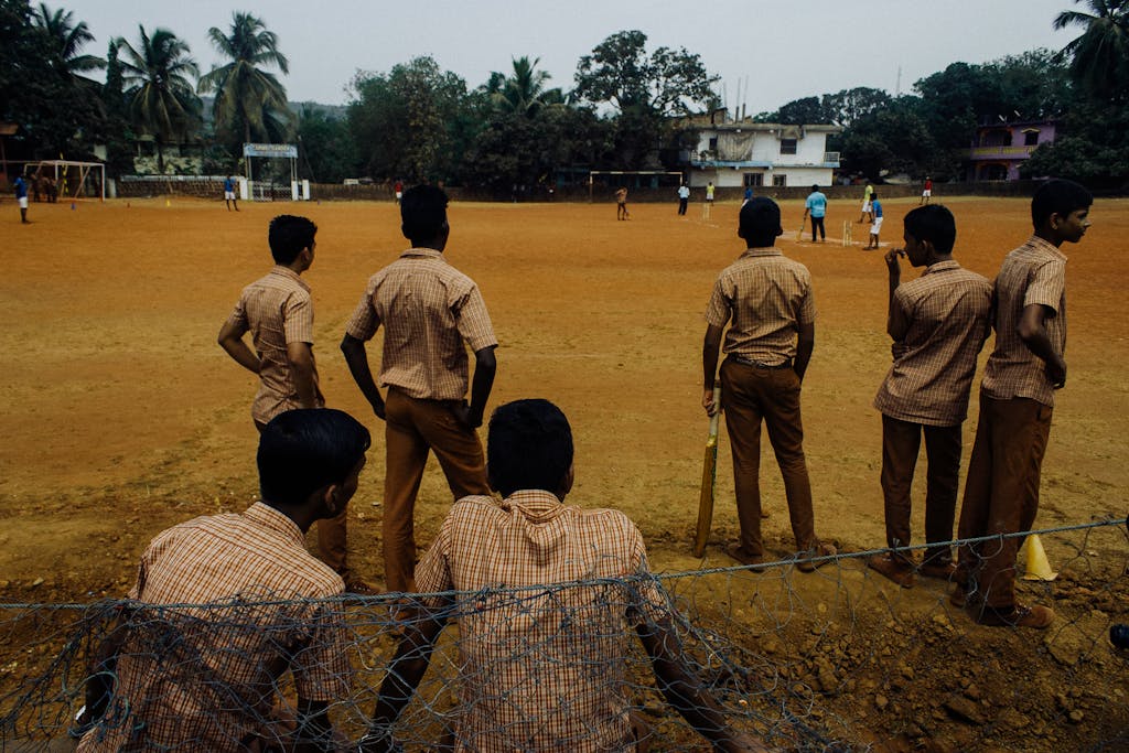 A group of students in uniforms playing cricket on a school ground under cloudy skies.