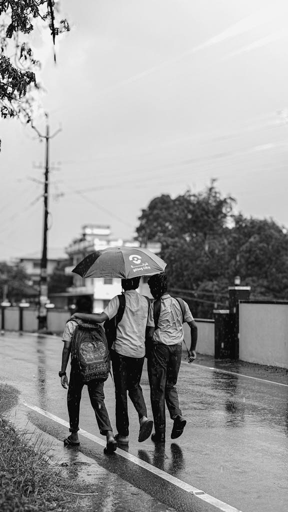 Three students walk in the rain with an umbrella on an Ernakulam street.